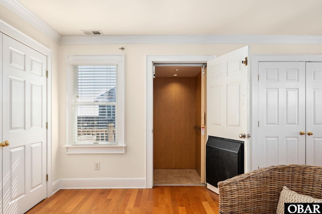 hallway featuring light wood finished floors, visible vents, crown molding, and baseboards