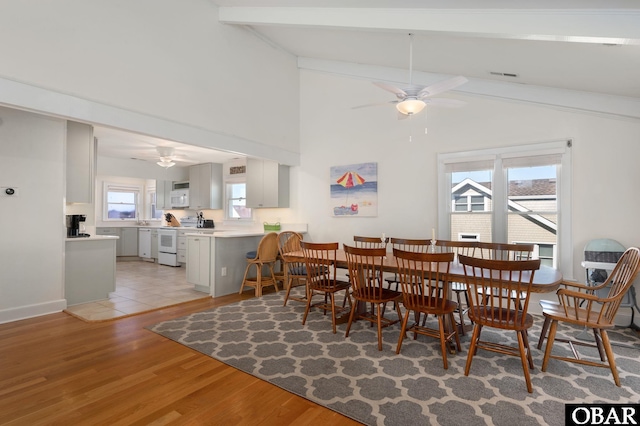 dining room featuring light wood finished floors, visible vents, vaulted ceiling with beams, and a ceiling fan