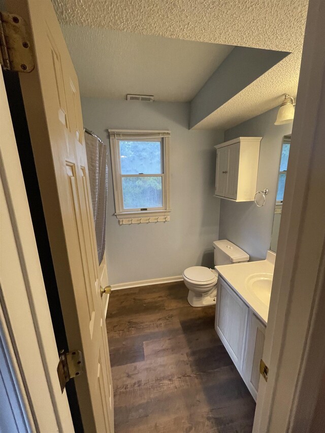 bathroom featuring visible vents, toilet, vanity, wood finished floors, and a textured ceiling