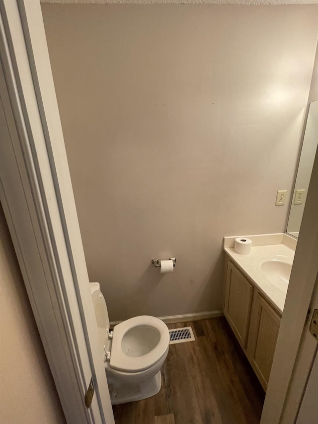 bathroom with vanity, wood finished floors, visible vents, baseboards, and toilet