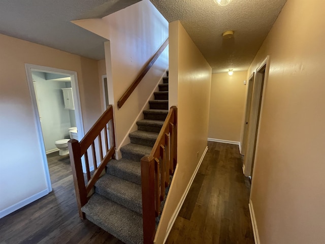 staircase with wood finished floors, baseboards, and a textured ceiling