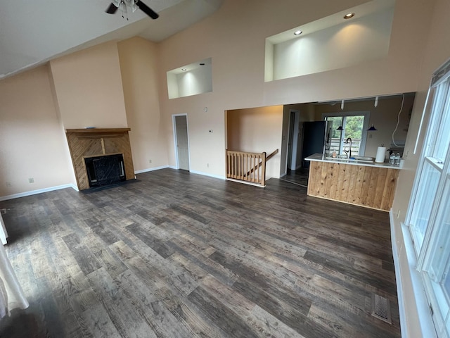 unfurnished living room featuring dark wood finished floors, a fireplace, visible vents, and a towering ceiling