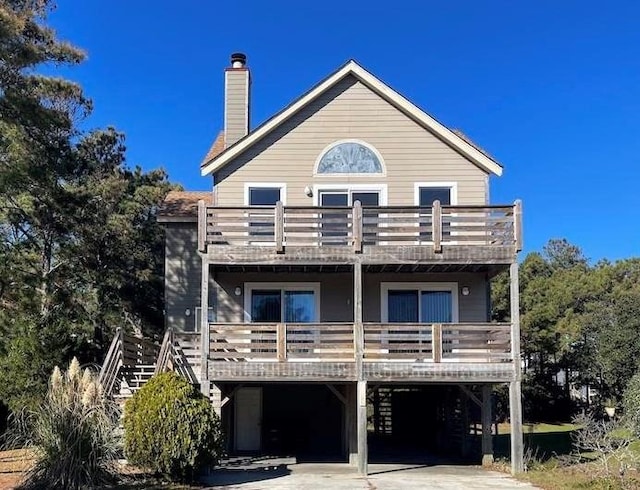 back of property with driveway, a balcony, stairway, a carport, and a chimney