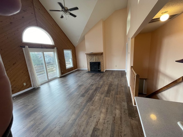 unfurnished living room with wooden walls, high vaulted ceiling, dark wood finished floors, a fireplace, and ceiling fan