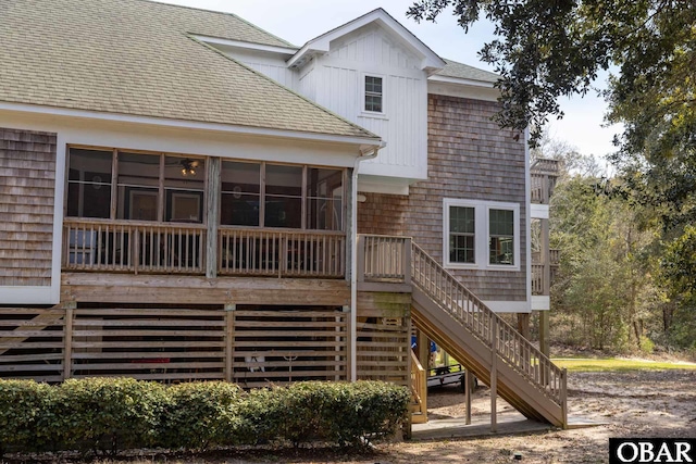 back of house featuring stairway, a sunroom, and a shingled roof