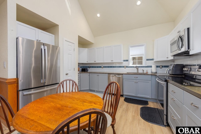 kitchen with tasteful backsplash, light wood-type flooring, lofted ceiling, appliances with stainless steel finishes, and a sink