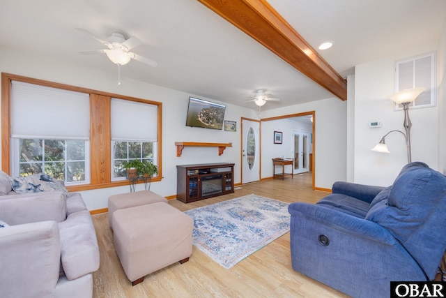 living area featuring wood finished floors, baseboards, a ceiling fan, a glass covered fireplace, and beamed ceiling