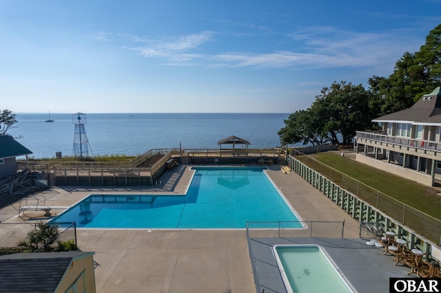 community pool featuring a patio area, fence, and a water view