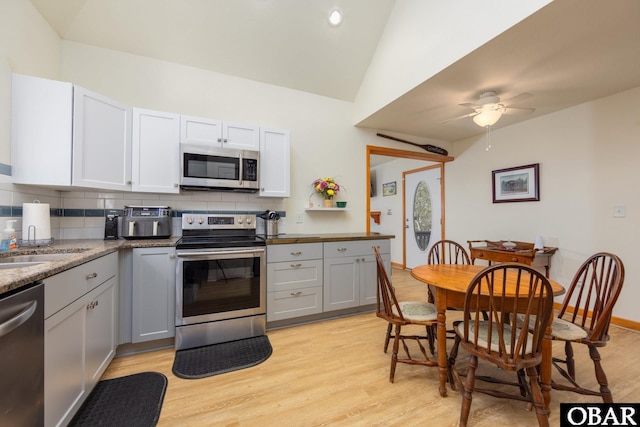 kitchen with light wood finished floors, gray cabinetry, vaulted ceiling, decorative backsplash, and stainless steel appliances