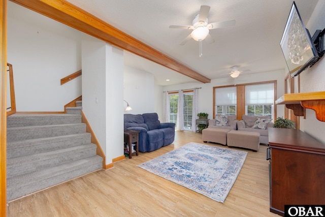 living room featuring beamed ceiling, a ceiling fan, wood finished floors, stairway, and baseboards