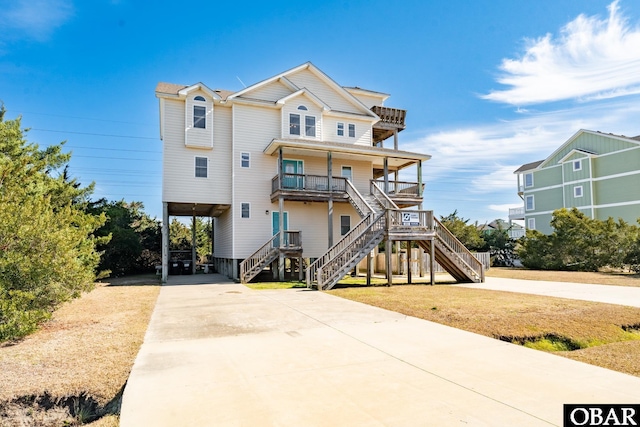 coastal home with a carport, stairs, a porch, and concrete driveway