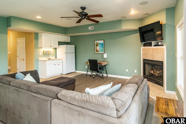 living area with a fireplace, visible vents, a ceiling fan, light wood-type flooring, and baseboards