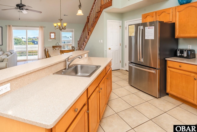 kitchen featuring light tile patterned floors, freestanding refrigerator, a kitchen island with sink, pendant lighting, and a sink