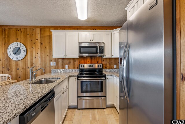 kitchen with light stone countertops, appliances with stainless steel finishes, white cabinets, and a sink