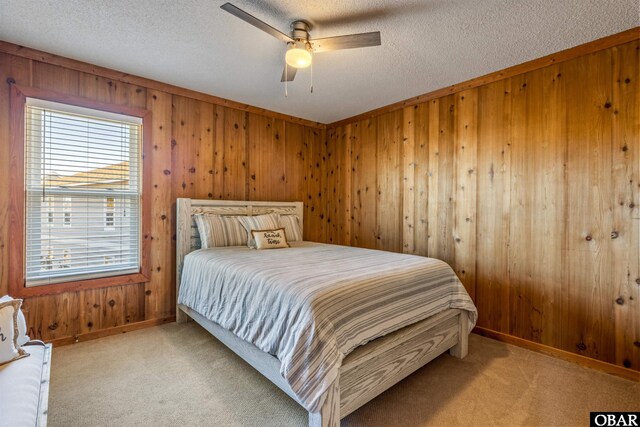 bedroom featuring a textured ceiling, wooden walls, ceiling fan, and light colored carpet