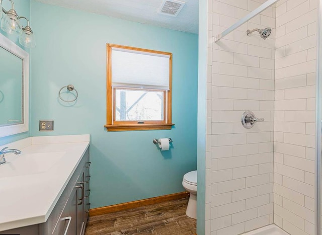 bathroom with visible vents, toilet, wood finished floors, and a tile shower