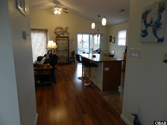 kitchen with a breakfast bar, dark wood-style flooring, dark countertops, lofted ceiling, and visible vents