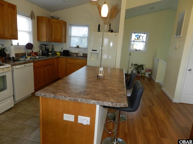 kitchen featuring pendant lighting, brown cabinets, vaulted ceiling, white appliances, and a kitchen breakfast bar