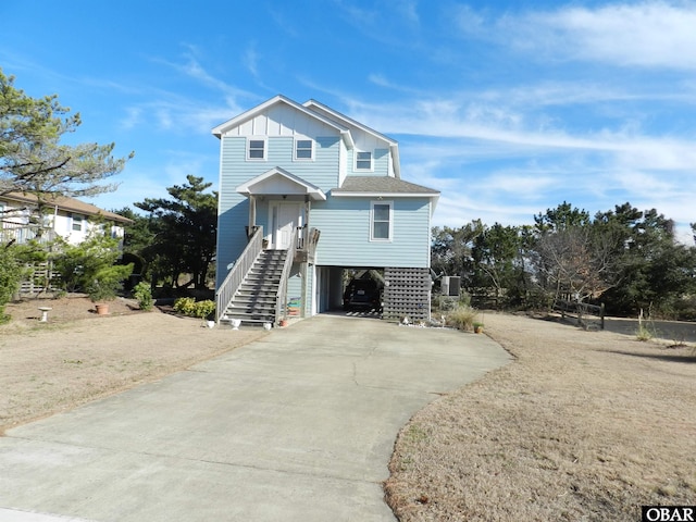 coastal home featuring roof with shingles, concrete driveway, board and batten siding, a carport, and cooling unit