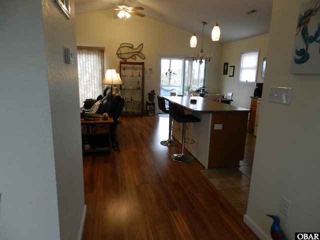 kitchen featuring dark wood-style flooring, a breakfast bar area, dark countertops, a kitchen island, and vaulted ceiling