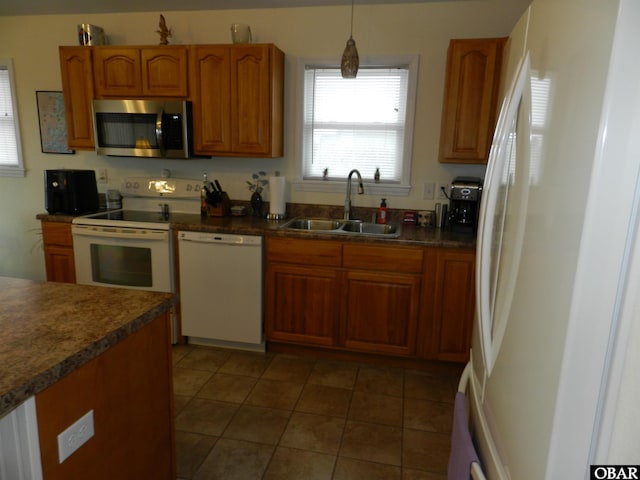 kitchen featuring dark countertops, hanging light fixtures, brown cabinetry, a sink, and white appliances