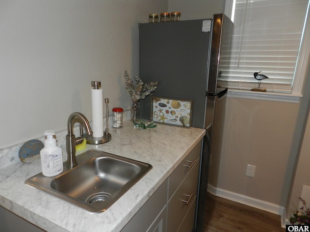 kitchen with dark wood-style floors, a sink, light stone countertops, and baseboards