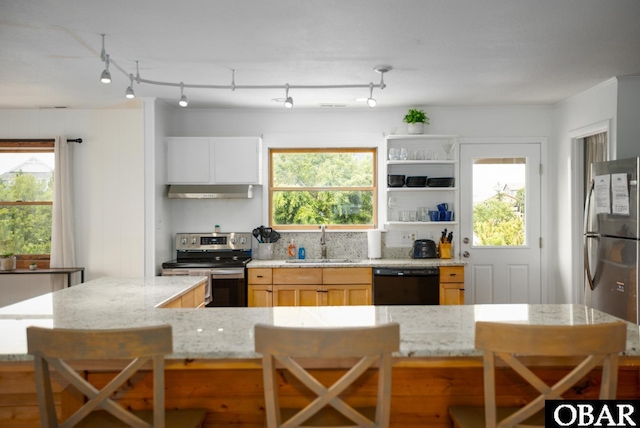 kitchen with light stone counters, open shelves, stainless steel appliances, a sink, and plenty of natural light