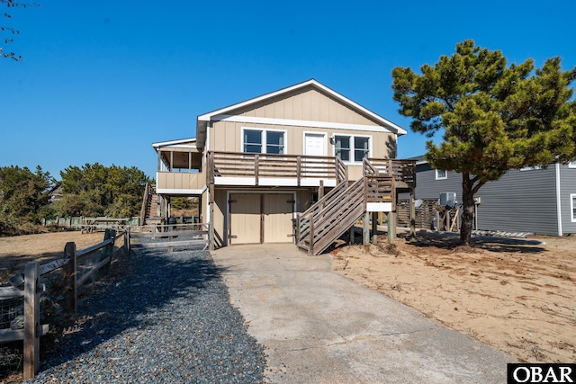 raised beach house with board and batten siding, driveway, fence, and stairs