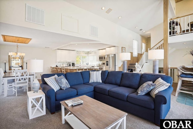 living room featuring carpet floors, stairs, visible vents, and an inviting chandelier