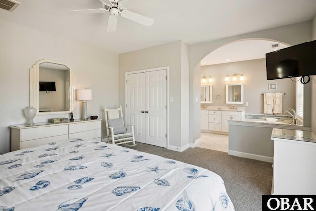 bedroom featuring a closet, connected bathroom, arched walkways, light carpet, and visible vents