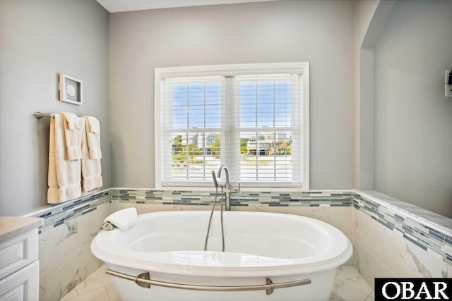 bathroom featuring tile walls, marble finish floor, a wealth of natural light, and a freestanding bath