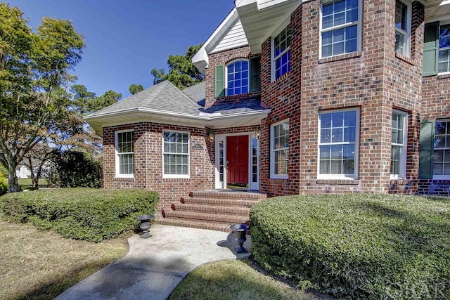 property entrance with a yard, a shingled roof, and brick siding