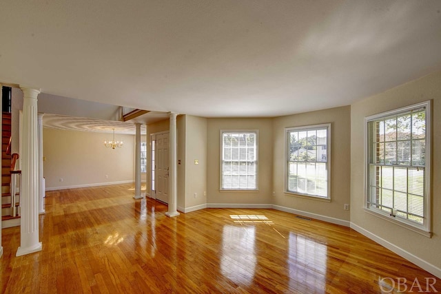 unfurnished living room with baseboards, an inviting chandelier, decorative columns, and light wood-style floors