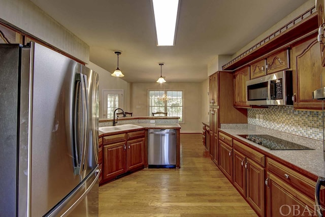 kitchen with a sink, light wood-style floors, light countertops, appliances with stainless steel finishes, and hanging light fixtures