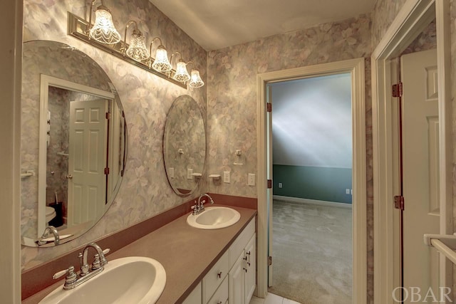 bathroom featuring double vanity, wallpapered walls, vaulted ceiling, and a sink