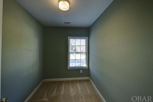 spare room with carpet floors, baseboards, visible vents, and a textured wall