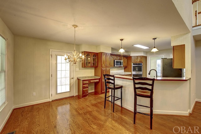 kitchen with light wood finished floors, brown cabinetry, glass insert cabinets, a breakfast bar, and stainless steel appliances