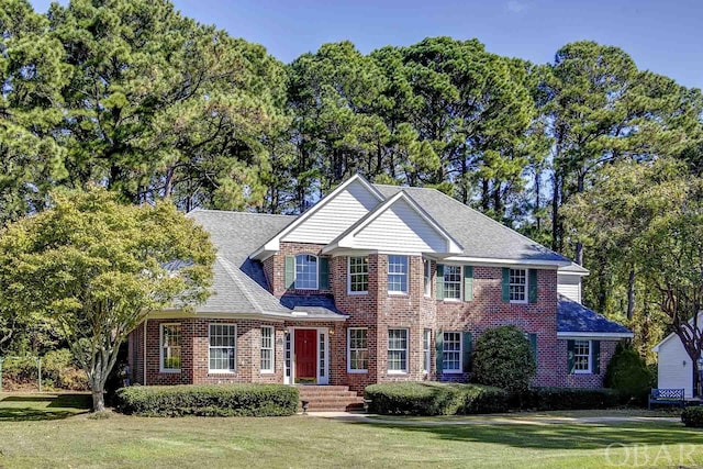 view of front of property with a front yard, brick siding, and roof with shingles