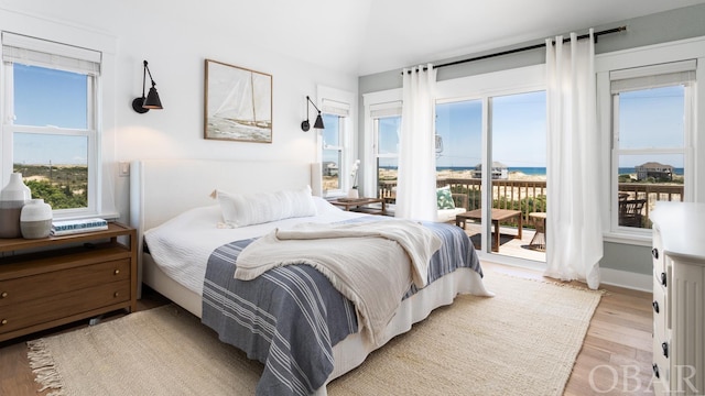 bedroom featuring a water view, access to exterior, multiple windows, and light wood-style floors