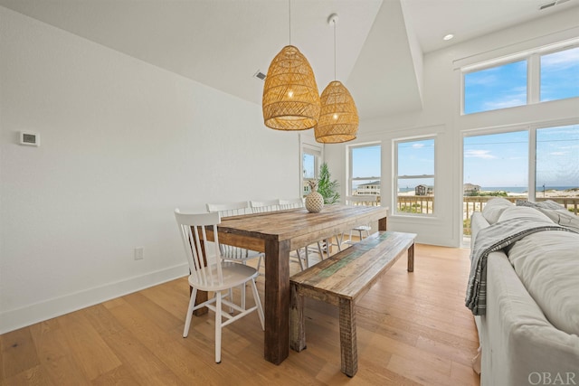 dining space with light wood-type flooring, high vaulted ceiling, visible vents, and baseboards