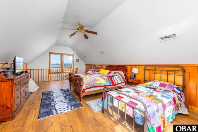 bedroom featuring lofted ceiling, wooden walls, visible vents, a ceiling fan, and light wood finished floors