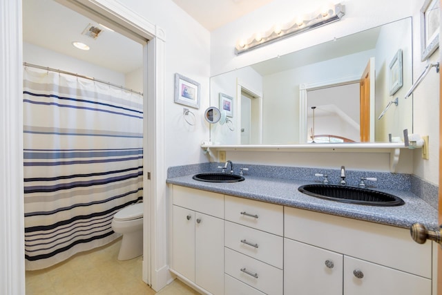 bathroom with toilet, double vanity, and a sink