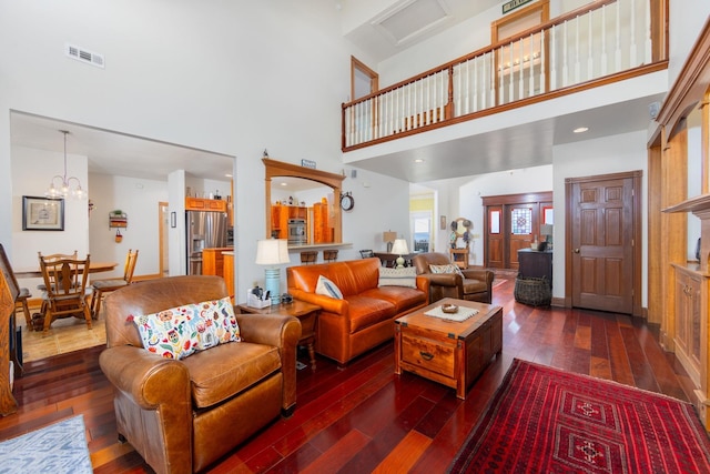 living area featuring dark wood-type flooring, a towering ceiling, visible vents, and a notable chandelier