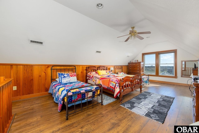 bedroom with visible vents, a ceiling fan, lofted ceiling, wood finished floors, and wood walls