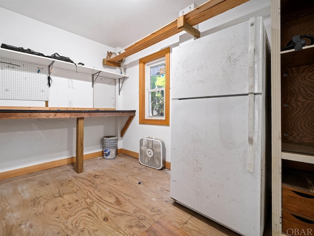 basement featuring baseboards, a workshop area, and freestanding refrigerator