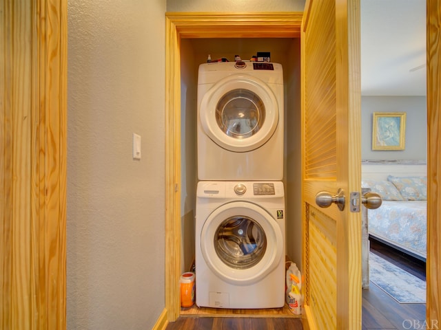 laundry area with stacked washer and dryer, laundry area, a textured wall, and dark wood-style flooring