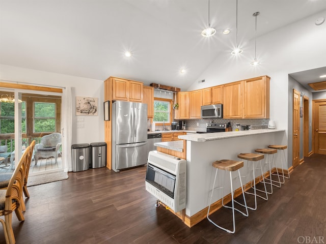 kitchen featuring appliances with stainless steel finishes, a breakfast bar, decorative light fixtures, heating unit, and a peninsula