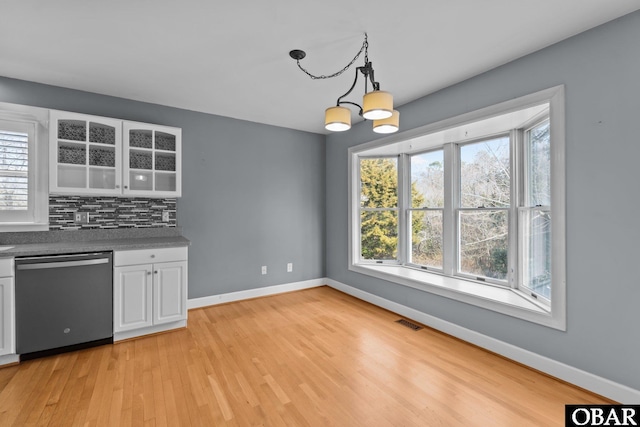 kitchen with baseboards, white cabinets, visible vents, stainless steel dishwasher, and backsplash