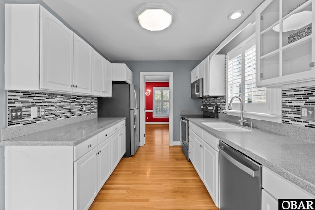 kitchen with light wood finished floors, stainless steel appliances, light countertops, white cabinetry, and a sink