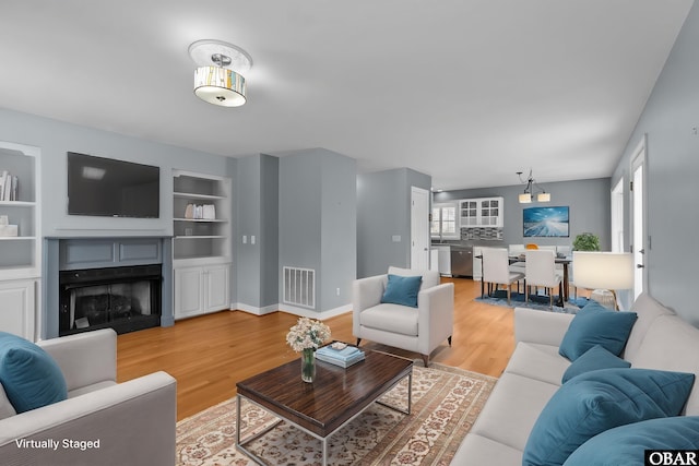 living room featuring baseboards, visible vents, light wood-type flooring, built in shelves, and a fireplace